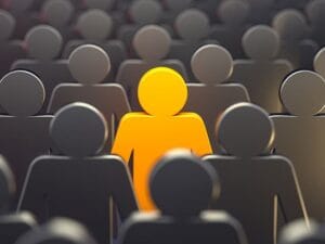 A group of grey humanoid figures with one standing out in bright orange in the center. The image symbolizes individuality and uniqueness.