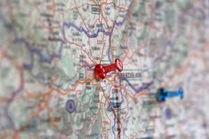 A close up of a red thumb tack pushed into a point on a street map