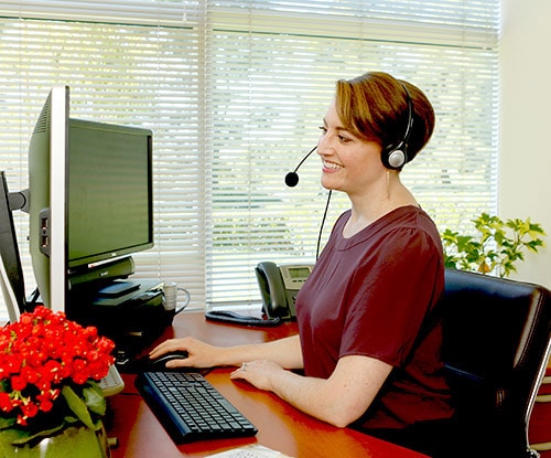 A Custom Dental Implant Marketing consultant helping a customer on the phone while working a her desk.